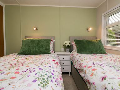 A bedroom with two single beds floral bedspreads green pillows a white nightstand with a flowerpot at Robins Lodge in White Cross Bay near Troutbeck Bridge
