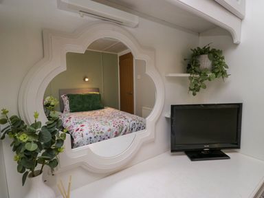 A bedroom reflected in a white decorative mirror with a television and plants on a white desk at Robins Lodge White Cross Bay near Troutbeck Bridge
