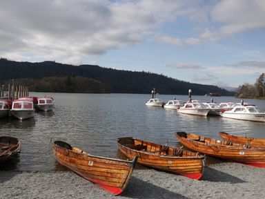 Wooden rowboats and white motorboats on a lake with forested hills in the background at Robins Lodge White Cross Bay near Troutbeck Bridge