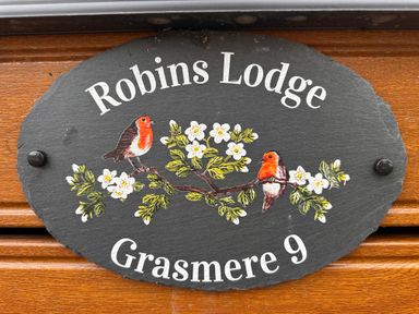 An oval black sign with two birds on a flowered branch and text robins lodge grasmere 9