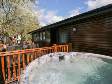 An outdoor deck with a hot tub and wicker chairs next to a wooden cabin at Robins Lodge in White Cross Bay near Troutbeck Bridge