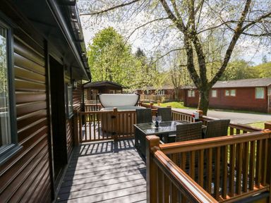 A wooden patio with a hot tub and a glass table with four chairs outside wooden lodges at Robins Lodge in White Cross Bay near Troutbeck Bridge