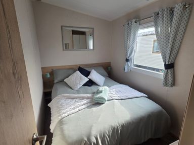 A bedroom with a double bed and a mirror at Pines 15 in Porthcawl