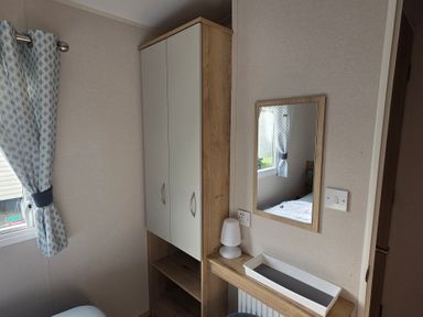 A bedroom with a cabinet, mirror, lamp, and shelf at Pines 15 in Porthcawl