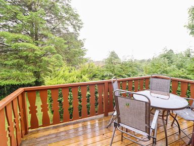An outdoor area with a wooden deck, table, and chairs at Y Bwthyn Pren, Cabin 209, Trawsfynydd