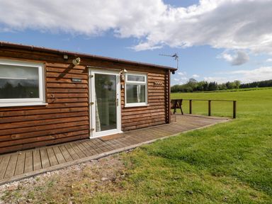 A wooden lodge with windows and a door opening onto a deck overlooking a grassy field at Twilight in Raglan