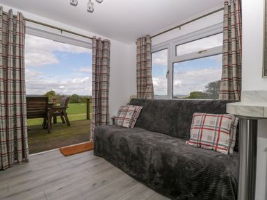 A living room with a dark sofa and plaid curtains next to a sliding door opening to a wooden deck with outdoor chairs at Twilight in Raglan