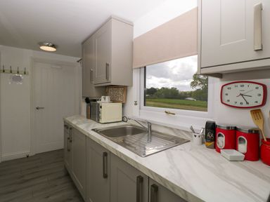 A kitchen with a marble countertop, sink, microwave, wall clock, and window showing an outdoor view at Twilight in Raglan