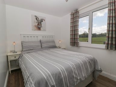 A bedroom with a double bed striped gray bedding bedside tables with lamps and a window with plaid curtains at Twilight in Raglan