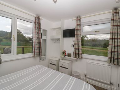A bedroom with a bed a television two windows with checked curtains and two bedside tables at Twilight in Raglan