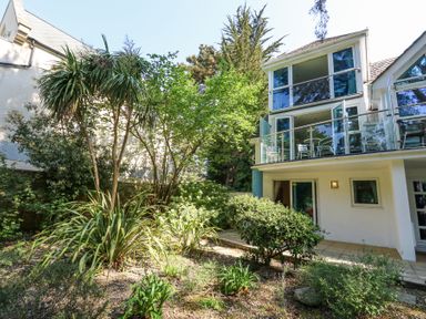 A modern house with large glass windows and balconies surrounded by various plants and trees at 6 Red Sails in Sandbanks