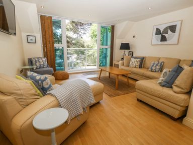 A living room with beige sofas a wooden coffee table and a glass door leading to a balcony at 6 Red Sails in Sandbanks