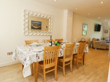 A dining area with a table set with plates glasses and a fruit bowl and wooden chairs at 6 Red Sails in Sandbanks
