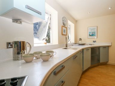 A kitchen with a curved countertop cups kettle sink and wall clock at 6 Red Sails in Sandbanks