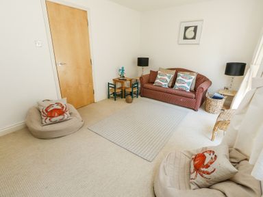 A living room with a sofa cushions with fish patterns small table and chairs and cushions with crab patterns at 6 Red Sails in Sandbanks