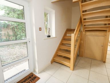 An entryway with a wooden staircase a white door with glass panels a small window with a seahorse ornament and tiled floor at 6 Red Sails in Sandbanks