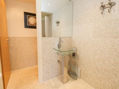 A bathroom with a glass sink pedestal a large mirror tiled walls and a shower area at 6 Red Sails in Sandbanks
