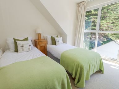 A bedroom with two single beds green blankets and a wooden nightstand with a lamp near a window at 6 Red Sails in Sandbanks