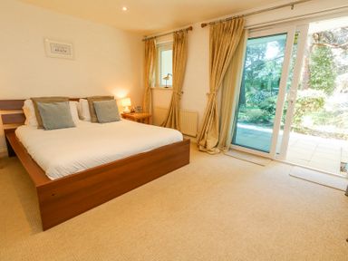 A bedroom with a wooden bed white bedding two pillows beige curtains and sliding glass door at 6 Red Sails in Sandbanks