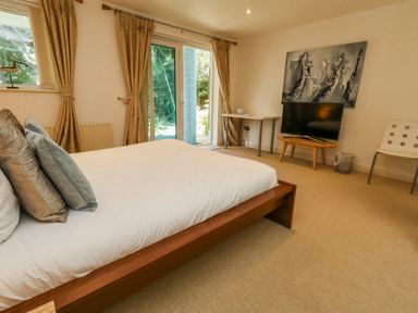 A bedroom with a bed cushions television on table and glass doors with curtains at 6 Red Sails in Sandbanks