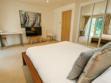 A bedroom with a bed pillows a chair a television on a wooden stand a white table and mirrored wardrobe doors at 6 Red Sails in Sandbanks