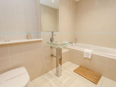 A bathroom with a glass sink on a metal pedestal bathtub with a towel and wooden mat on the floor at 6 Red Sails in Sandbanks