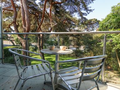 A balcony with two metal chairs and a round table with two cups overlooking trees and greenery at 6 Red Sails in Sandbanks