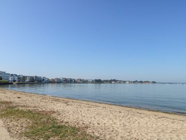 A sandy beach with calm water and buildings along the shoreline at 6 Red Sails in Sandbanks