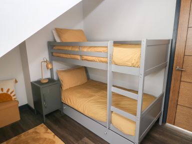 A bunk bed with yellow bedding and a nightstand in the bedroom at 10 Brython Place Tackley