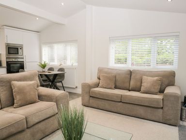 A living room with two beige sofas and a small dining table with chairs near a kitchen at Mere Brook Lodge in White Cross Bay