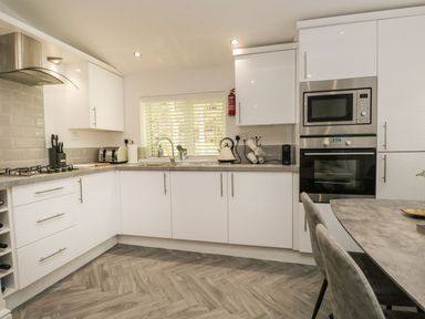 A modern kitchen with white cabinets a gas stove built in microwave and oven a sink under a window and a dining table with chairs at Mere Brook Lodge in White Cross Bay