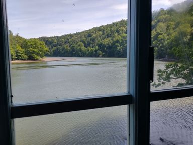 A view from a window overlooking water and trees at The Sharpham Boat House in Ashprington