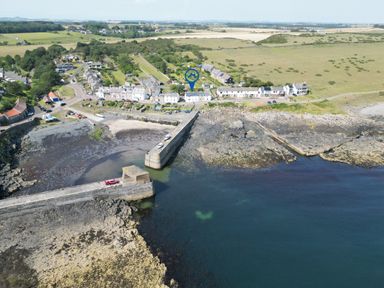 An aerial view of a village near the coast with a pier and parked vehicles at Puffin Cottage in Craster