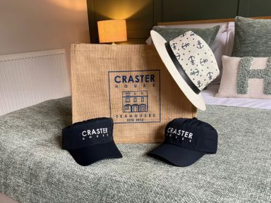 A hat and caps with a bag on a bed at Craster House Seahouses