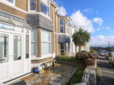 A row of houses along a street with parked cars and a stone patio with a bench at Breakers Point in St Ives