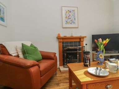 A living room with a leather armchair a wooden coffee table flowers on the table a fireplace and a television at Breakers Point in St Ives