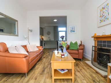 A living room with brown leather sofas a wooden coffee table with flowers and scones and a fireplace at Breakers Point in St Ives