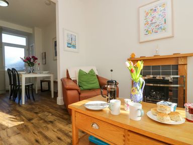 A sitting area with a brown leather chair green cushion wooden coffee table with mugs and scones and a dining table with chairs in a room at Breakers Point in St Ives