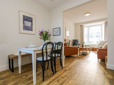 A dining area with a table set for four and a living room with sofas and a television at Breakers Point in St Ives