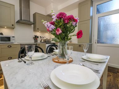 A kitchen with a dining table set with plates glasses and cutlery and flowers in a vase at Breakers Point in St Ives