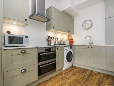 A kitchen with beige cabinets a microwave oven stove washing machine and a wall clock at Breakers Point in St Ives