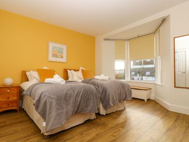 A bedroom with two single beds a wooden bedside table a bay window with blinds and a wall mirror at Breakers Point in St Ives