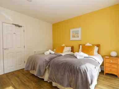 A bedroom with two single beds a yellow wall a bedside table and a door at Breakers Point in St Ives