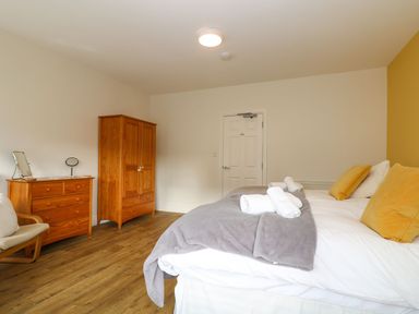 A bedroom with a bed having yellow pillows and gray blankets wooden wardrobe and chest of drawers with two mirrors at Breakers Point in St Ives