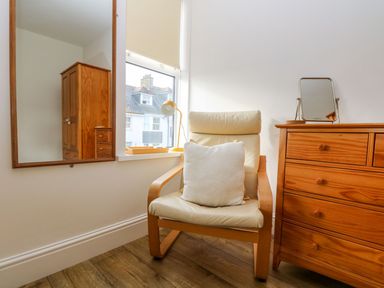 A chair with a cushion next to a wooden dresser and mirror in a room at Breakers Point in St Ives