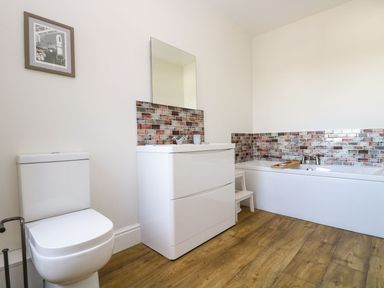 A bathroom with a toilet sink cabinet mirror bathtub with tile backsplash and wooden floor at Breakers Point in St Ives