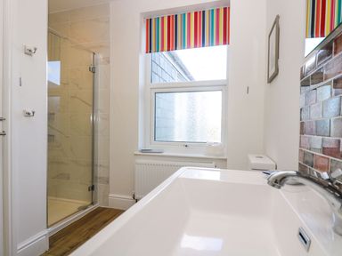 A bathroom with a shower enclosure a window with a striped blind and a sink with a faucet at Breakers Point in St Ives
