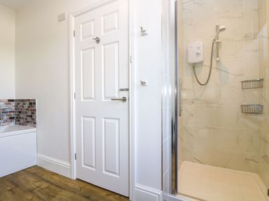 A bathroom with a shower enclosure a white door and a bathtub with mosaic tiles at Breakers Point in St Ives