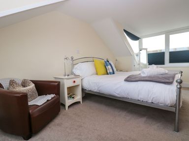 A bedroom with a metal bed frame a white nightstand a brown leather chair and windows at Breakers Point in St Ives