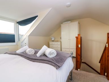 A bedroom with a bed covered with towels and a blanket near a window wardrobe and chest of drawers with mirrors at Breakers Point in St Ives